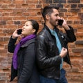 Young man and woman stand nearby back to back, talking on their cell phones Royalty Free Stock Photo