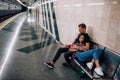 Young man and woman use underground. Couple in subway. Sitting and lying on bench. Empty metro station. Love story Royalty Free Stock Photo