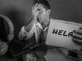 Young messy and depressed business man showing notepad asking for help desperate and sad at office laptop computer desk looking ov Royalty Free Stock Photo