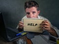 Young messy and depressed business man showing notepad asking for help desperate and sad at office laptop computer desk looking ov Royalty Free Stock Photo