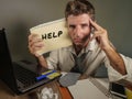 Young messy and depressed business man showing notepad asking for help desperate and sad at office laptop computer desk looking ov Royalty Free Stock Photo