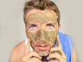 Young messy funny man looking at himself horrified in bathroom mirror with green cream on his face applying beauty facial mask pro