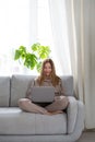 Young or middle age woman sitting with laptop on grey couch in home office. Concept of remote workplace and working at Royalty Free Stock Photo