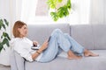 Young or middle age woman sitting with laptop on grey couch in home office with monstera plant. Concept of remote Royalty Free Stock Photo