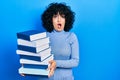 Young middle east woman holding a pile of books afraid and shocked with surprise and amazed expression, fear and excited face Royalty Free Stock Photo