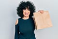 Young middle east woman holding take away paper bag looking positive and happy standing and smiling with a confident smile showing Royalty Free Stock Photo