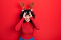 Young middle east woman wearing cute christmas reindeer horns doing ok gesture like binoculars sticking tongue out, eyes looking