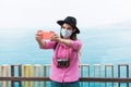 Young millenial woman making a vlog with her smartphone while wearing a protective mask during her travel for coronavirus spread