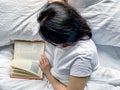 Young millennial candid woman reading red book at home on white striped bedsheets. Early morning. Text in book is Royalty Free Stock Photo