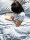 Young millennial candid woman reading red book at home on white striped bedsheets. Early morning. Text in book is Royalty Free Stock Photo