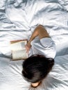 Young millennial candid woman reading red book at home on white striped bedsheets. Early morning. Text in book is Royalty Free Stock Photo