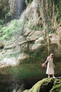 Young millennial woman in dress and beige hat stands in forest happy and relaxed, enjoys nature and tranquility. Travel