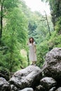 Young millennial woman in dress and beige hat stands in forest happy and relaxed, enjoys nature and tranquility. Travel