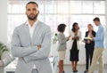 Young mixed race businessman standing with arms crossed while in an office with colleagues. Serious hispanic male boss Royalty Free Stock Photo