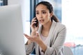 Young mixed race businesswoman on a call using her phone and desktop computer making a hand gesture looking worried in Royalty Free Stock Photo