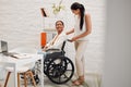 Young mixed race businesswoman helping a colleague in a wheelchair to her office at work. Hispanic businessperson with a Royalty Free Stock Photo