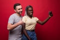 Young mixed race couple, caucasian man and african woman taking selfie from phone while standing on red background Royalty Free Stock Photo