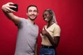 Young mixed race couple, caucasian man and african woman taking selfie from phone while standing on red background Royalty Free Stock Photo