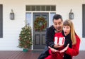 Young Mixed Race Couple Exchanging Gift On Front Porch of House with Christmas Decorations Royalty Free Stock Photo