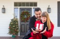 Young Mixed Race Couple Exchanging Gift On Front Porch of House with Christmas Decorations