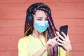 Young mixed race girl with dreadlocks listening music on headphones while wearing face mask Royalty Free Stock Photo