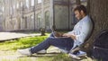 Young mixed-race guy using laptop under tree, smiling at good news, emotions