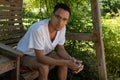 Young mixed race man looking directly into camera, seated on a backyard swing with greenery background Royalty Free Stock Photo