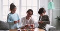 Young mixed race nanny teaching little kids creating handmade bracelets.