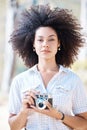 Young mixed race woman with curly hair taking creative photos on a vintage retro film camera. One female photographer