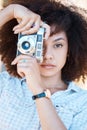 Young mixed race woman with curly hair taking creative photos on a vintage retro film camera. One female photographer