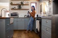 Young mixed race woman drinking a cup of coffee while using her phone alone in the morning in the kitchen. One hispanic Royalty Free Stock Photo