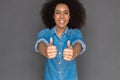 Freestyle. Mulatto woman standing on grey showing thumbs up close-up blurred smiling toothy