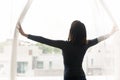 Young mixed race woman standing near window opening curtains. Royalty Free Stock Photo