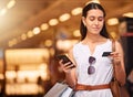 A young mixed race woman using a cell phone and bank card while carrying bags during a shopping spree. Young brunette Royalty Free Stock Photo