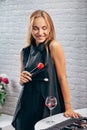 A young model girl in black clothes with her arms open holds a make-up brush and next is a glass of red wine. She smiles Royalty Free Stock Photo