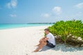 Young model handsome man in white t-shirt sitting on sandy beach at tropical island luxury resort