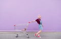 Young model poses with a cart on the background of a purple wall Royalty Free Stock Photo