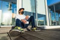 Young modern bored guy sitting on the ground in the city street leaning against a store window wearing Coronavirus protective mask Royalty Free Stock Photo