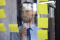 Young modern business man using adhesive notes while standing behind the glass wall in the office Royalty Free Stock Photo