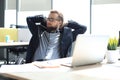 Young modern businessman keeping hands behind head and smiling while sitting in the office