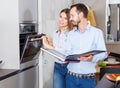 Young modern couple standing with recipe book in stylish kitchen near oven