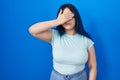 Young modern girl with blue hair standing over blue background covering eyes with hand, looking serious and sad Royalty Free Stock Photo