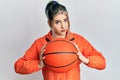Young modern girl holding basketball ball skeptic and nervous, frowning upset because of problem