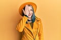 Young modern girl wearing yellow hat and leather jacket covering one eye with hand, confident smile on face and surprise emotion Royalty Free Stock Photo