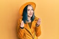 Young modern girl wearing yellow hat and leather jacket doing money gesture with hands, asking for salary payment, millionaire