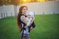 Young modern happy mom with baby son in ergo backpack walking in Sunny summer day. Concept of the joy of motherhood Royalty Free Stock Photo