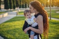 Modern happy mother with baby son in ergo backpack walking in Sunny summer day. Concept of the joy of motherhood Royalty Free Stock Photo