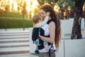 Young happy mother with baby son in ergo backpack walking in Sunny summer day. Concept of the joy of motherhood Royalty Free Stock Photo