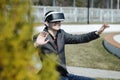 Young modern man wearing virtual reality glasses in a city park sits in a park on a bench and manipulates his hands, playing with Royalty Free Stock Photo