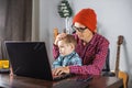 Modern man is working on a laptop, and his little son is sitting on his lap. Concept of family and remote work from home Royalty Free Stock Photo